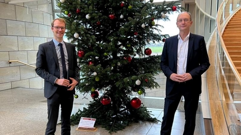 Dr. Christian Untrieser (links) und Dr. Klaus Wiener (rechts) stehen vor einem festlichen geschmückten Tannenbaum mit roten Weihnachtskugeln.