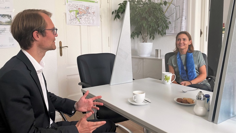 Dr. Bettina Warnecke und Dr. Christian Untrieser reden miteinander. Sie sitzen sich an einem Schreibtisch gegenüber.