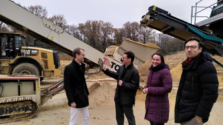 Christian Untrieser und drei Miterabeiter/innen der Firma Stremmer Sand + Kies GmbH. Im Hintergrund gelb-brauner Sand und Maschinen zur Förderung von Sand.