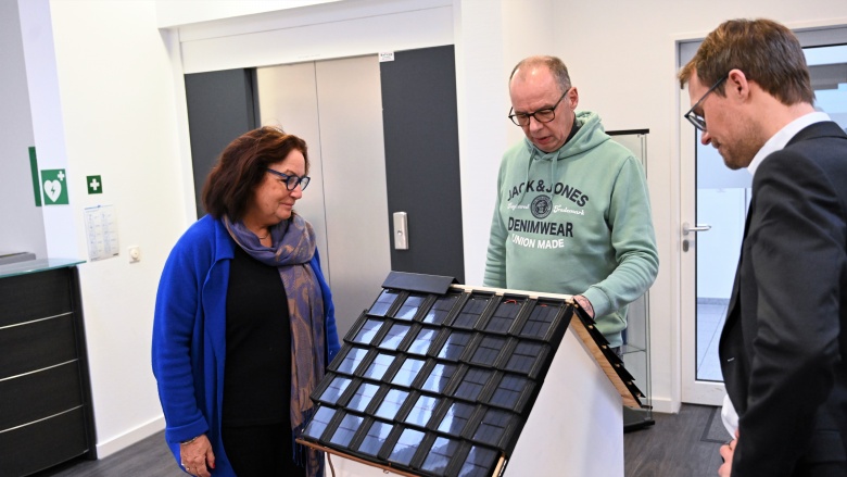 v.l.n.r.: Claudia Schlottmann MdL, Peter Hakenberg (Geschäftsführer der Firma paXos) und Christian Untrieser betrachten interessiert ein Miniaturdach-Modell, das mit schwarzen Solardachpfannen gedeckt ist.