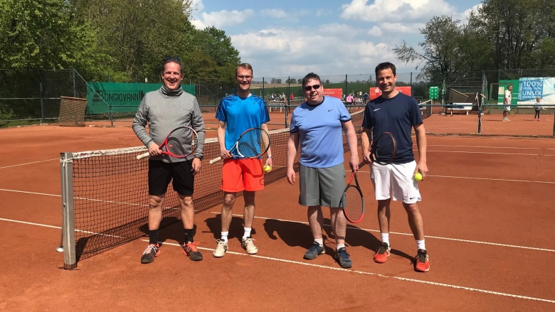 Dr. Christian Untrieser (2.v.l) in sportlicher Kleidung auf dem Tennisplatz des TC Grün-Weiß Hochdahl. Um ihn herum stehen drei weitere männliche Spieler. Alle halten Tennisschläger in der Hand. Im Hintergrund: Bäume und ein Tennisnetz.