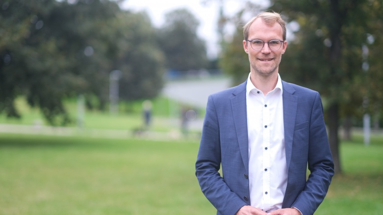 Dr. Christian Untrieser steht auf grüner Wiese. Er lächelt und trägt ein dunkelblaues Jackett und ein weißes Hemd. Im Hintergrund: grüne Laubbäume