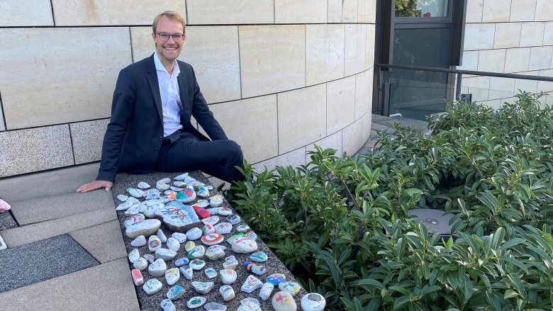 Dr. Christian Untrieser sitzt vor dem Landtag mit den bemalten Wunschsteinen der Städtischen Gesamtschule Haan.