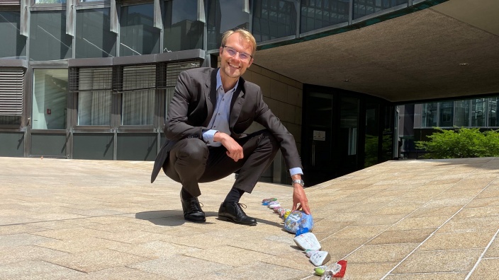 Dr. Christian Untrieser kniet fröhlich vor dem Landtag Düsseldorf neben einer Reihe bunt bemalter Steine.