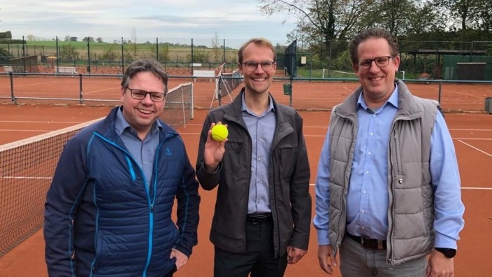 v.l.n.r.: Christoph Schilz, Dr. Christian Untrieser und Ansgar Schnepel stehen lächelnd auf dem Tennisplatz. Dr. Untrieser hält einen Tennisball in der Hand. Im Hintergrund Bäume und grüne Wiese
