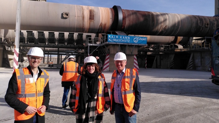 v.l.n.r.: Dr. Christian Untrieser, Ina Besche-Krastl und Martin Sträßer stehen vor großen Stahlrohren der Firma Lhoist in Wülfrath. Sie tragen weiße Schutzhelme und orange Warnwesten