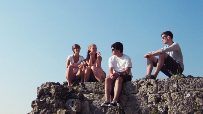 Gruppe Jugendliche sitzen bei schönem, sommerlichem Wetter auf einem Felsen
